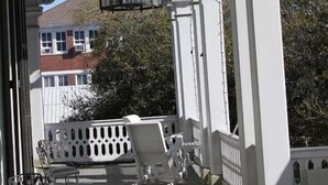 A covered porch with white columns, a hanging lantern, and outdoor furniture. - The Dansereau House (Thibodaux)