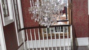 A grand staircase with a white balustrade, a chandelier, and a patterned carpet. - The Dansereau House (Thibodaux)