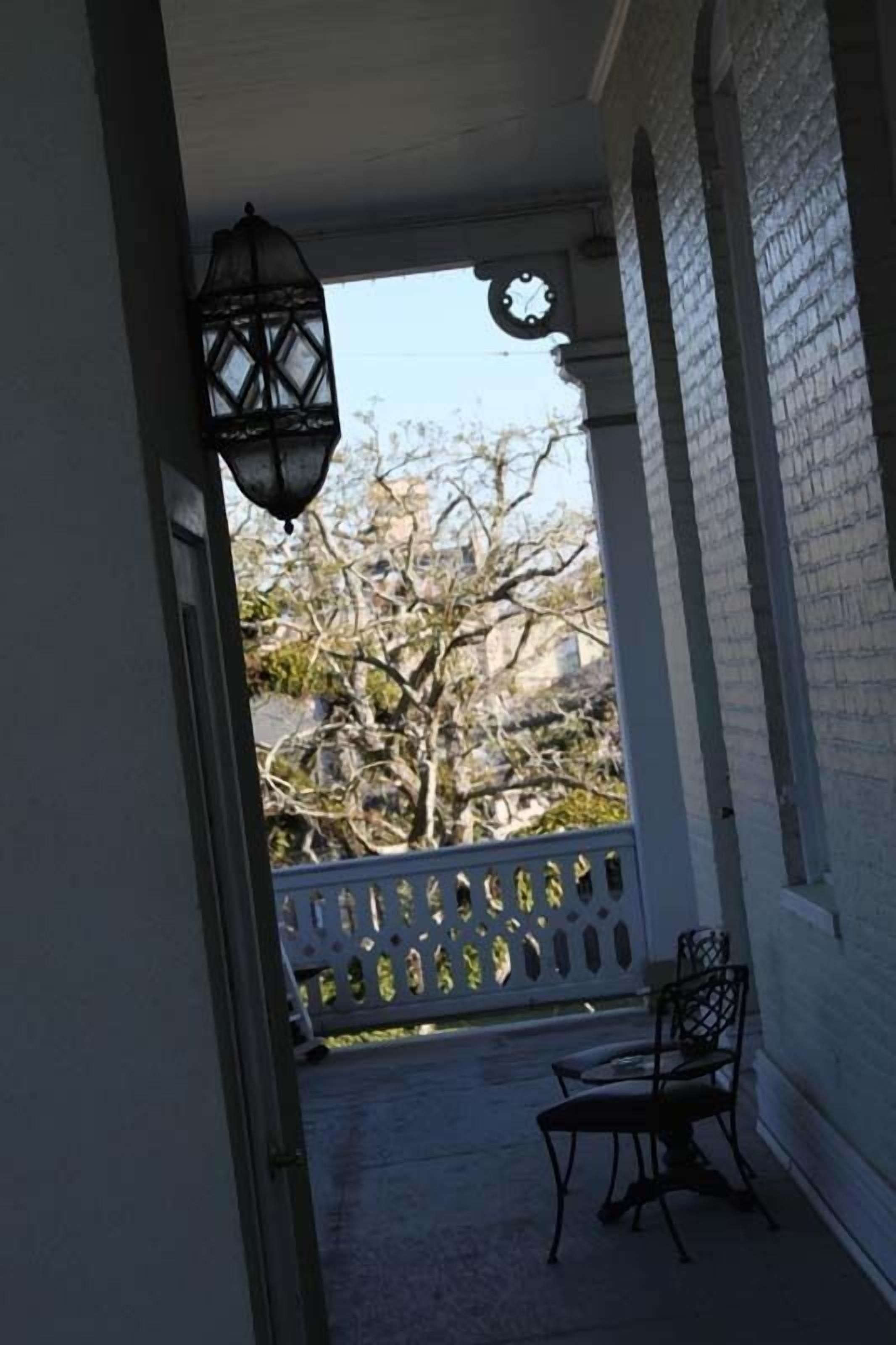 Une véranda couverte avec une clôture en treillis blanche, une chaise en métal et une lanterne suspendue.