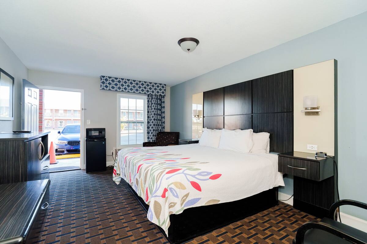 A hotel room with a large bed, a desk, a chair, a microwave, and a view of the street.