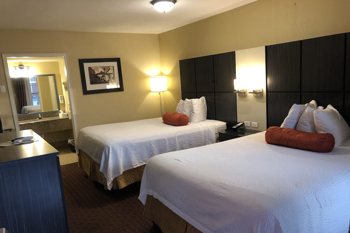 A hotel room with two beds, a desk, a mirror, and a framed picture on the wall.