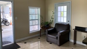 Une pièce aux murs de couleur beige, avec un fauteuil en cuir marron, une petite table sur laquelle est posée une plante, et une fenêtre donnant sur un bâtiment à l’extérieur.