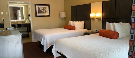 A hotel room with two beds, a desk, a mirror, and a picture on the wall.