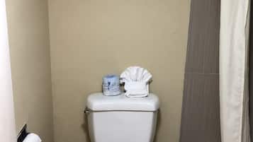 Une petite salle de bain comprenant des toilettes, une étagère avec des serviettes, une poubelle et un rideau de douche.
