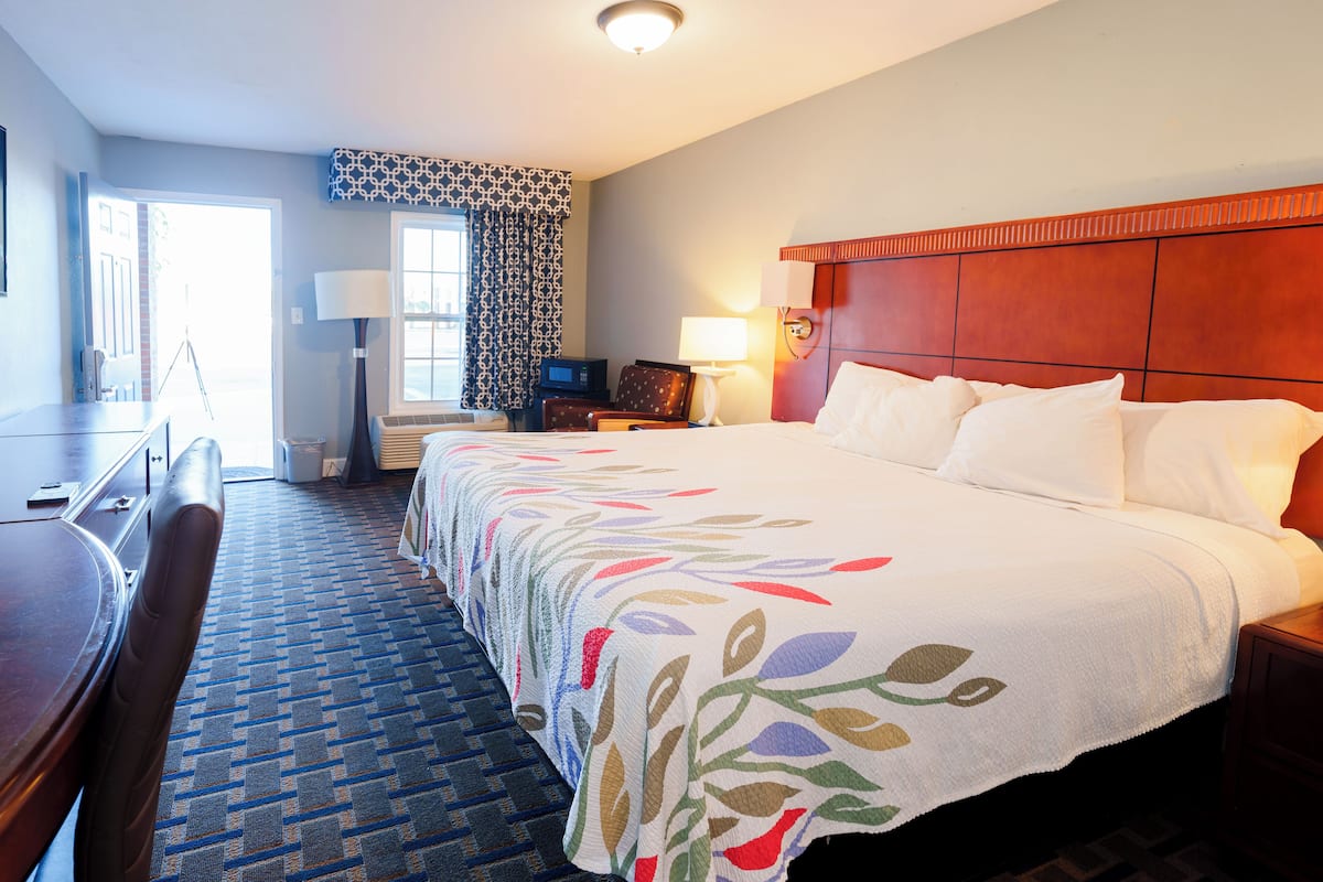 A hotel room with a large bed, a desk, a chair, a lamp, and a window with curtains.