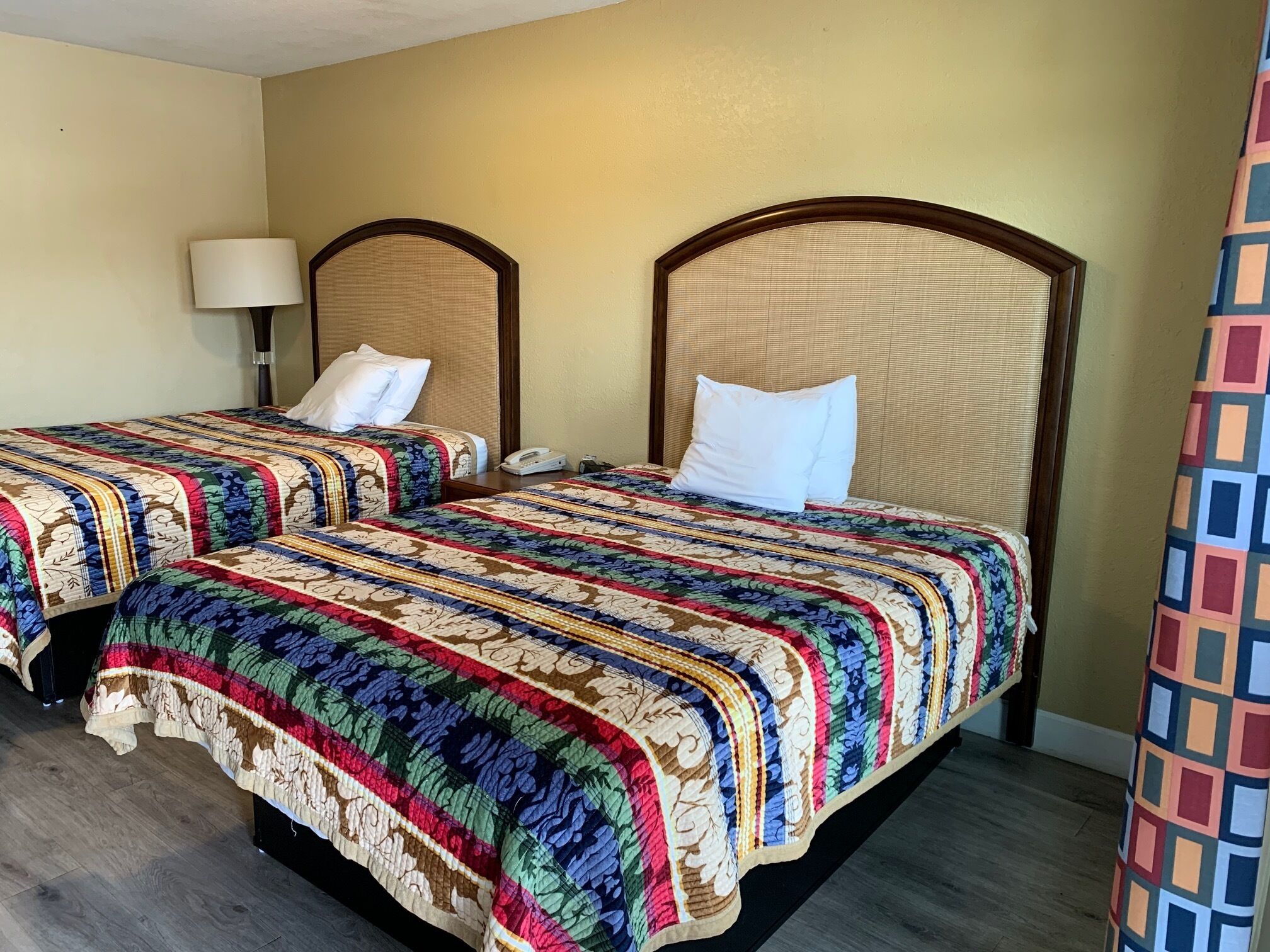A hotel room with two beds, each with a patterned bedspread and a wooden headboard.