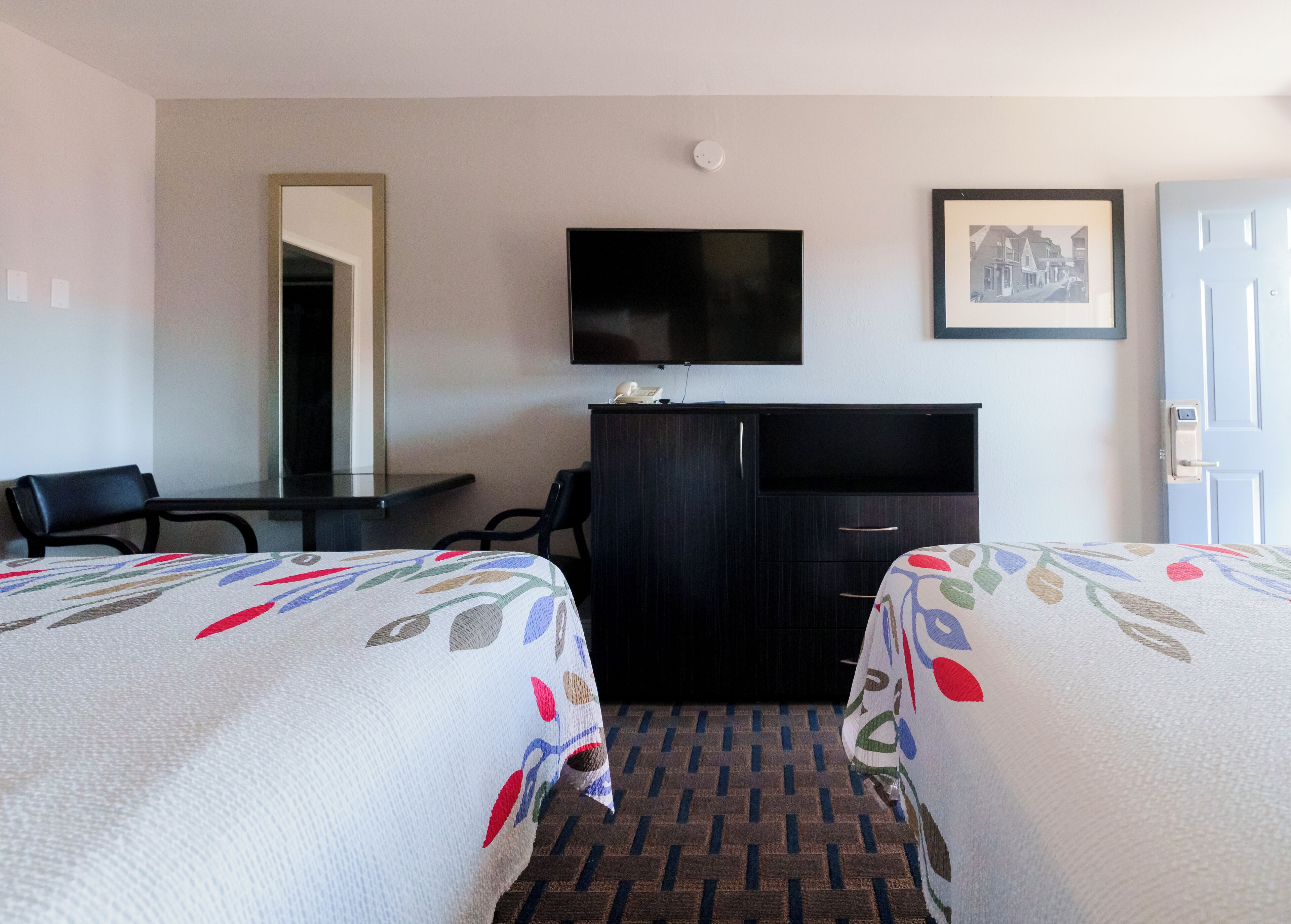 A hotel room with two beds, a desk, a chair, a television, a wardrobe, and a door.