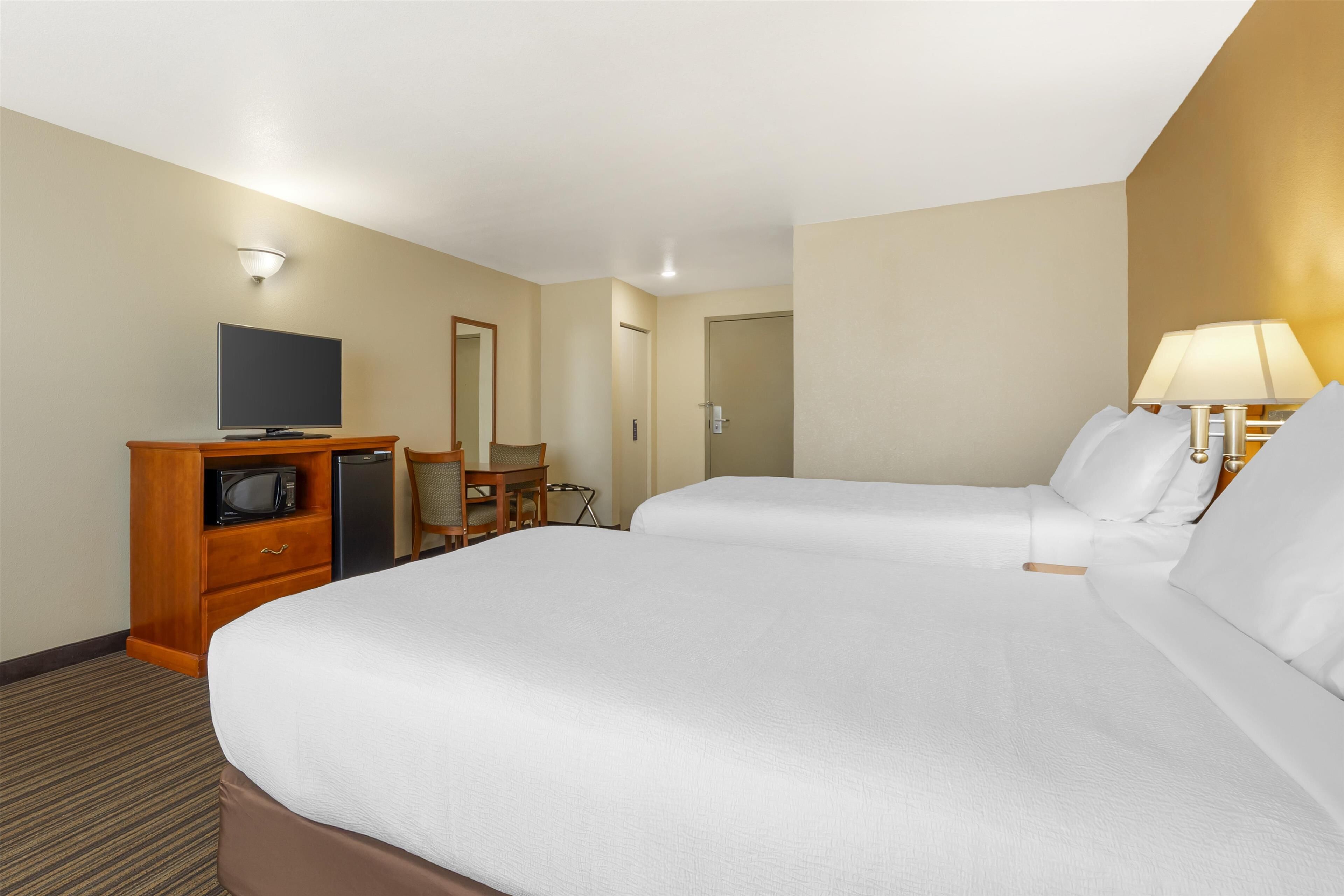 A hotel room with two beds, a TV, a desk, and a lamp.