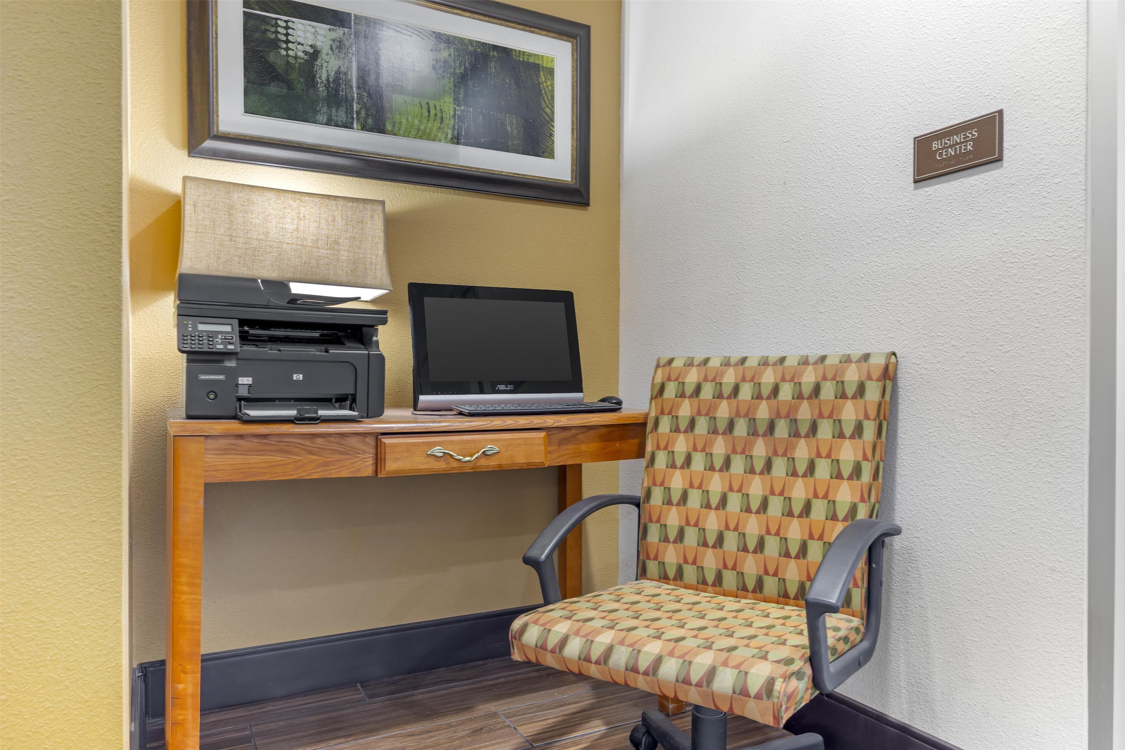 A desk with a laptop, printer, and lamp, a patterned chair, and a 'Business Center' sign on the wall.