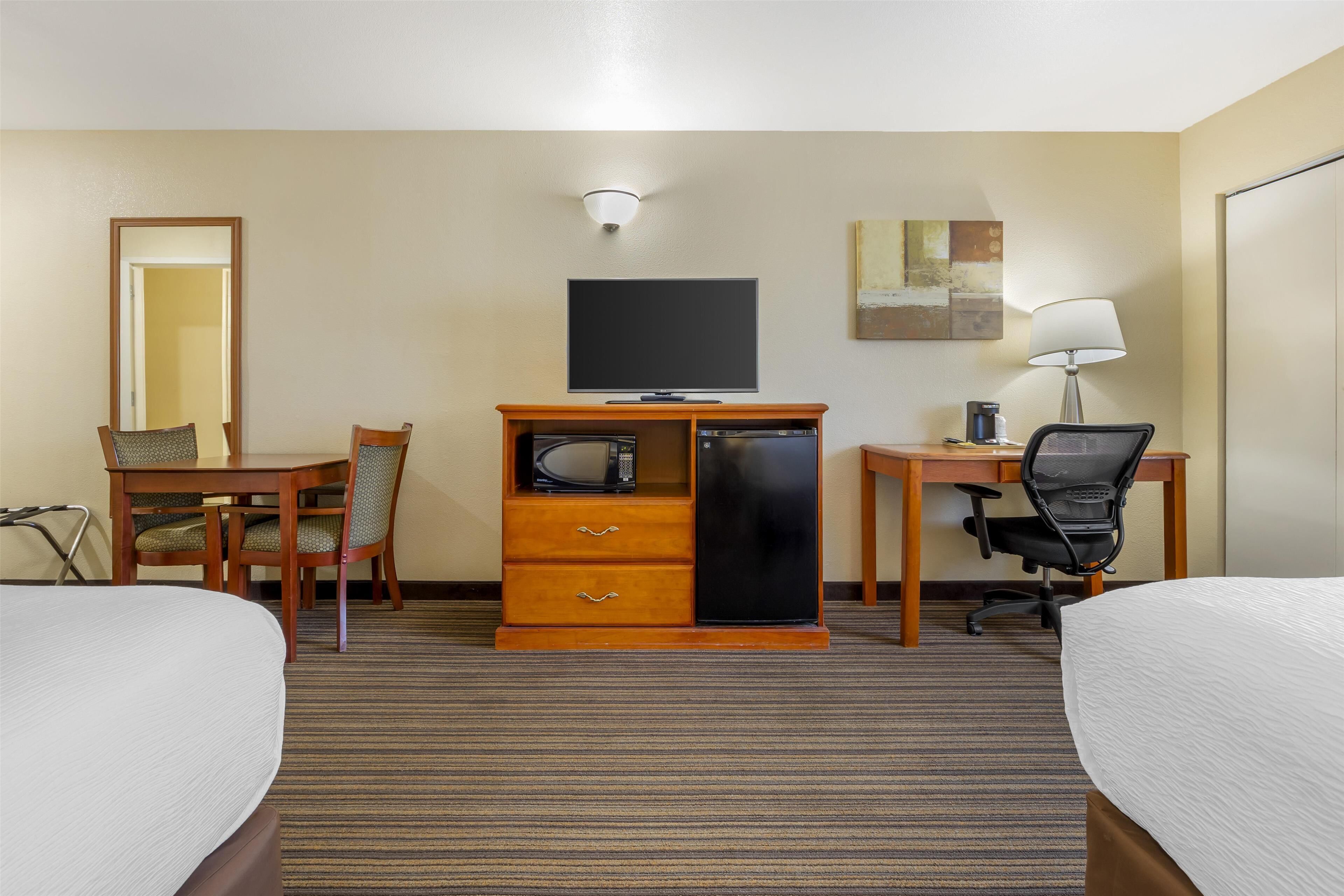 Una habitación de hotel con dos camas, un escritorio con computadora, televisor, microondas y un mueble pequeño.
