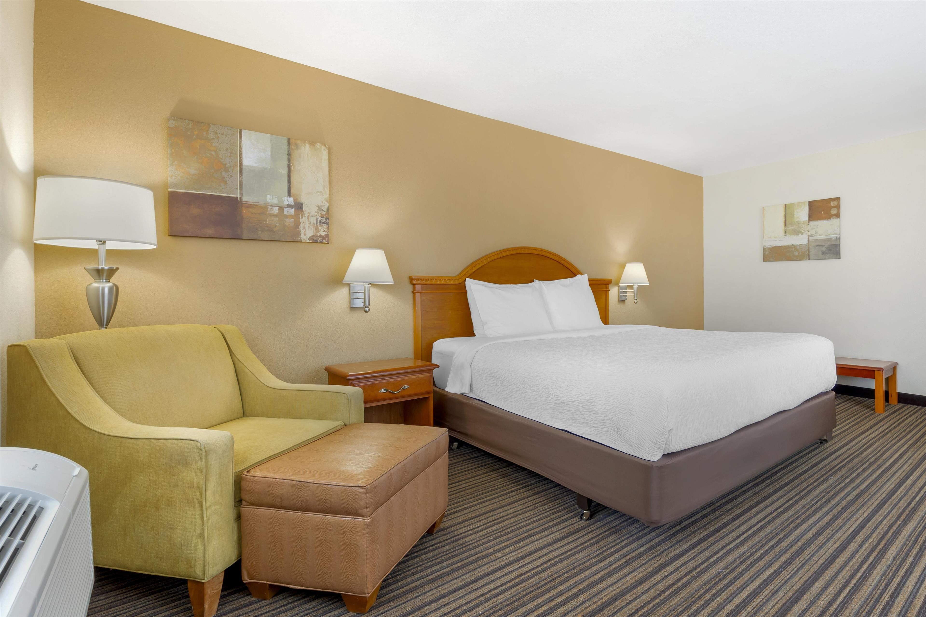 Ein Hotelzimmer mit einem Bett, einem Sessel, einem Nachttisch und einer Lampe.