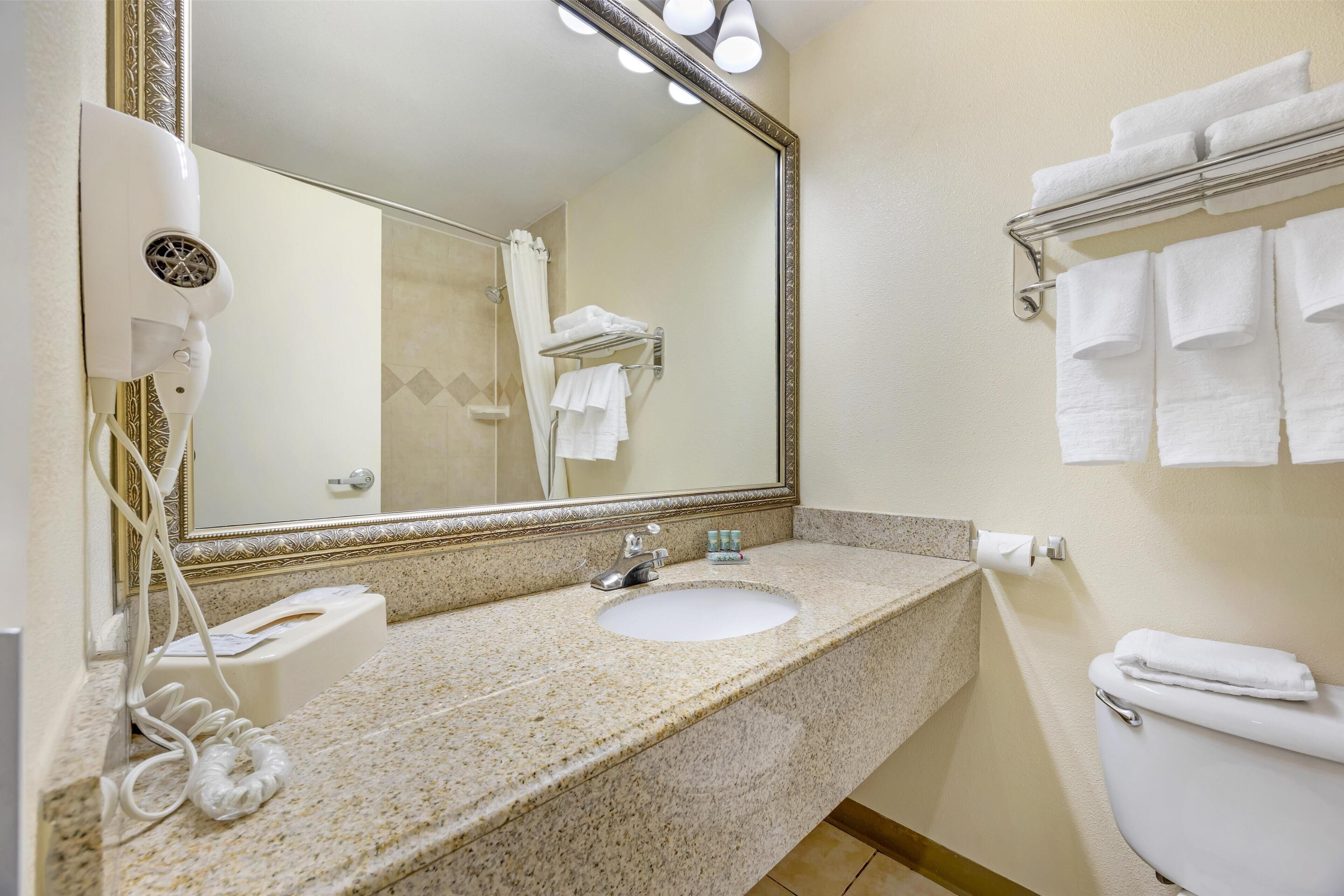 A bathroom with a granite countertop, a sink, a mirror, a hairdryer, and a towel rack.