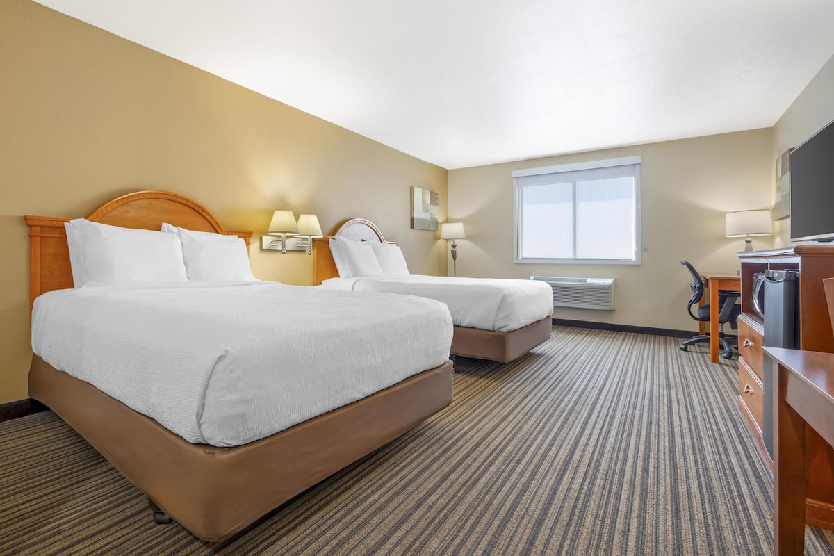 A hotel room with two beds, a desk, a television, and a window.