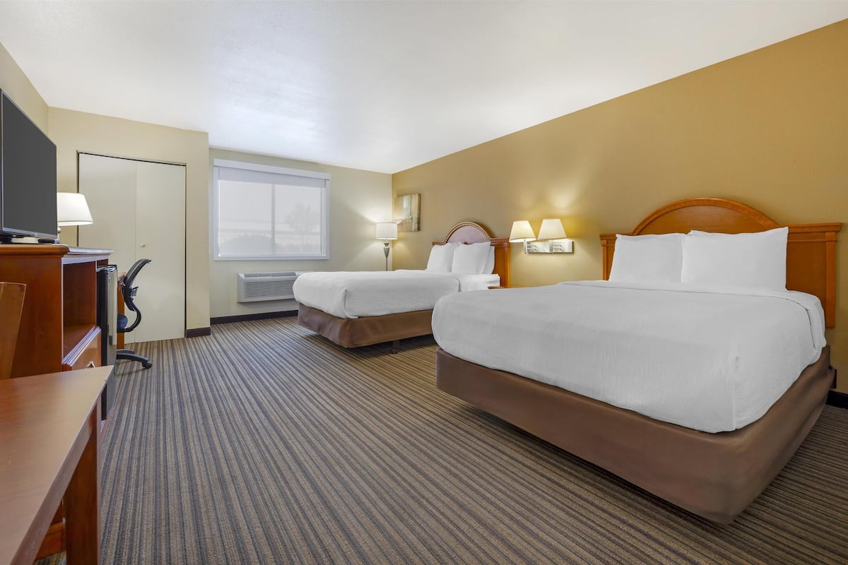 A hotel room with two beds, a desk, a television, and a window.