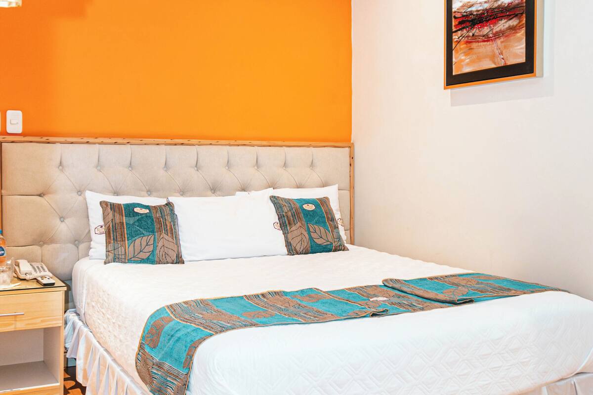 Un dormitorio con una cama, una mesita de noche, un teléfono y un cuadro en la pared.