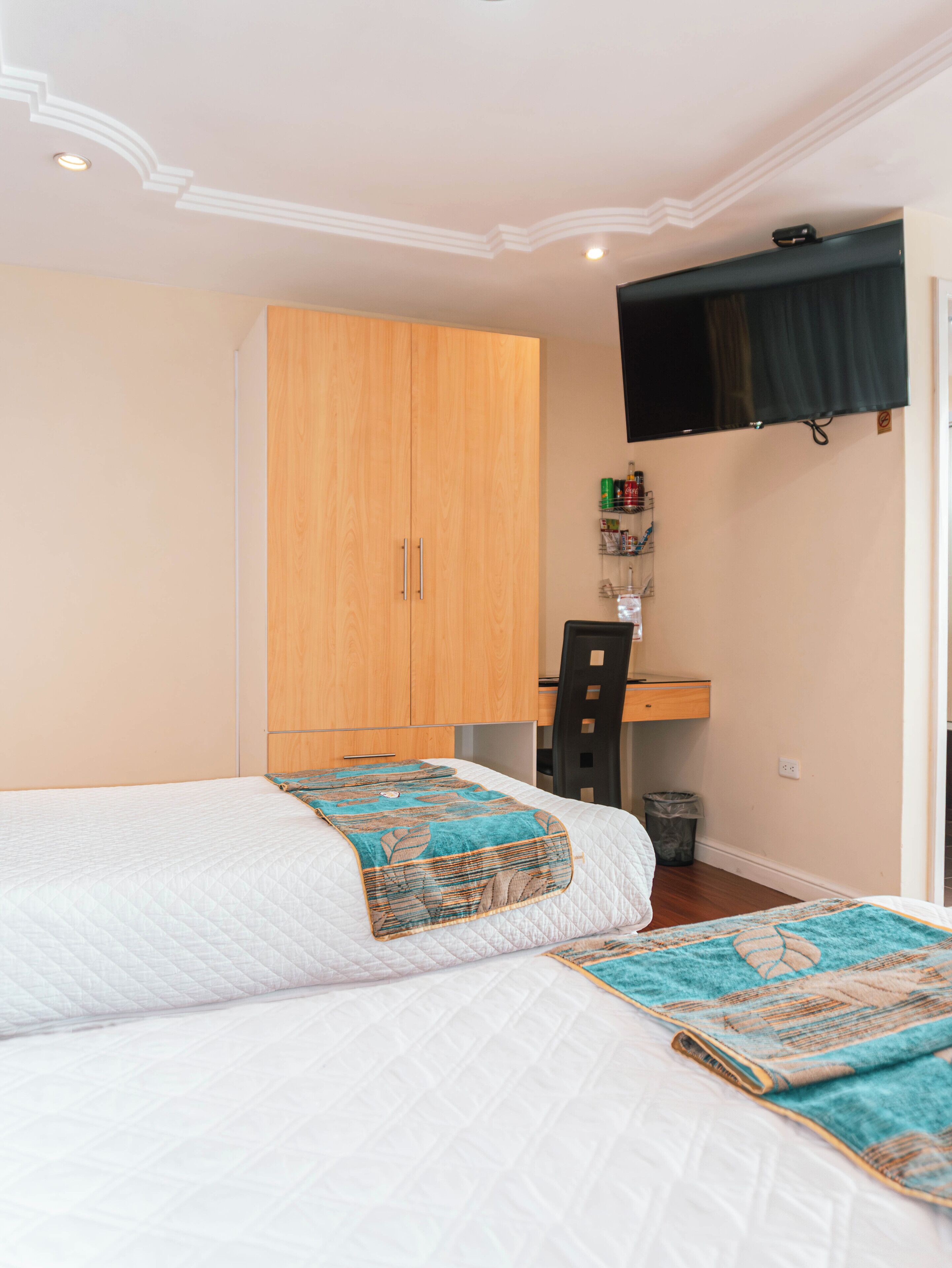 Un dormitorio con cama, armario de madera, escritorio con silla y televisor montado.