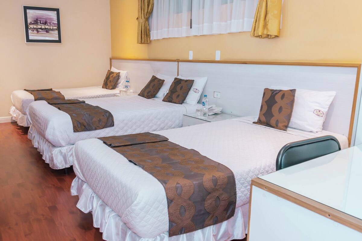 Habitación de hotel con tres camas individuales, un escritorio y una mesita.