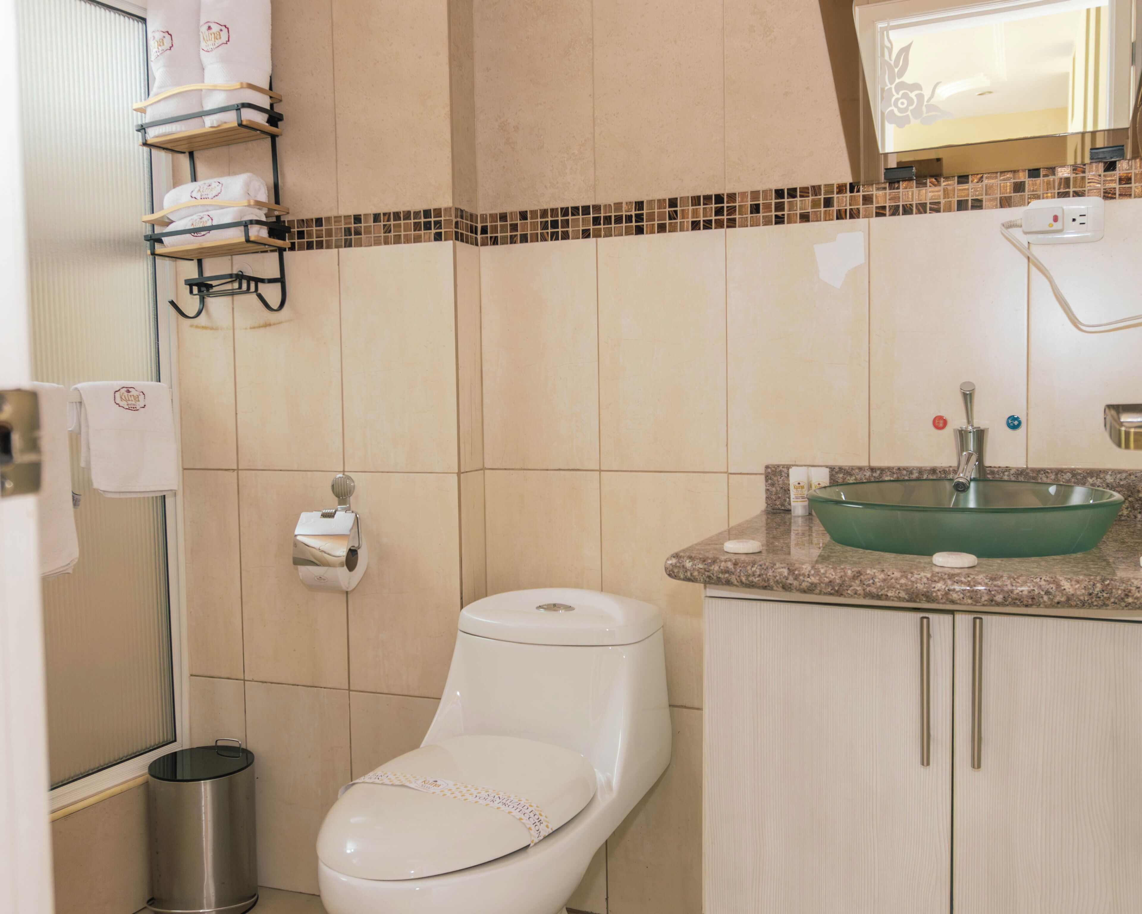 Un baño con inodoro, lavamanos, cubo de basura y toallero.