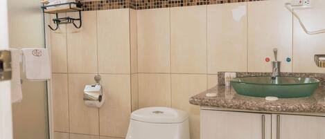 Un baño con inodoro, lavamanos, cubo de basura y toallero.