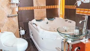 Een badkamer met een bad, toilet, glazen wastafel en een houten kastje.