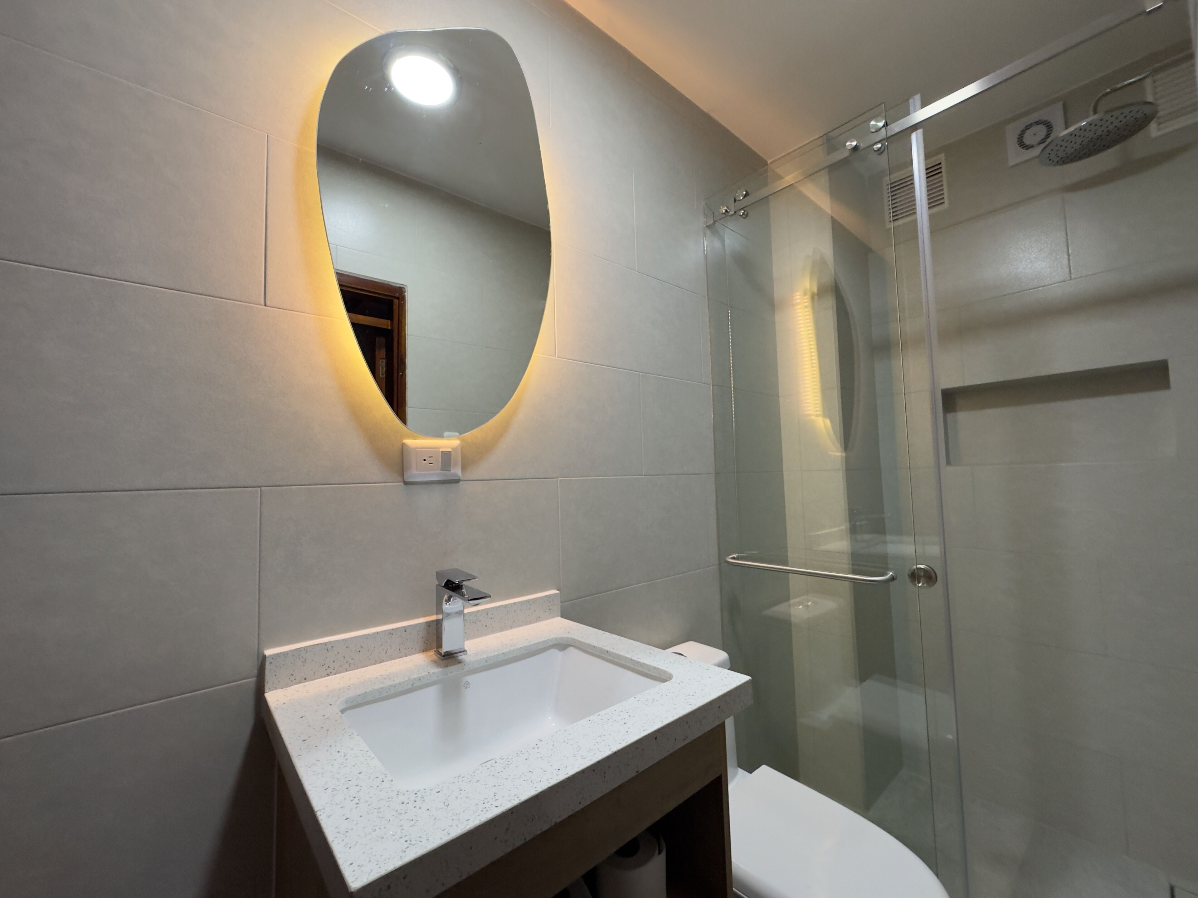 Un baño con cabina de ducha de vidrio, un lavamanos blanco con espejo y una lámpara de pared.