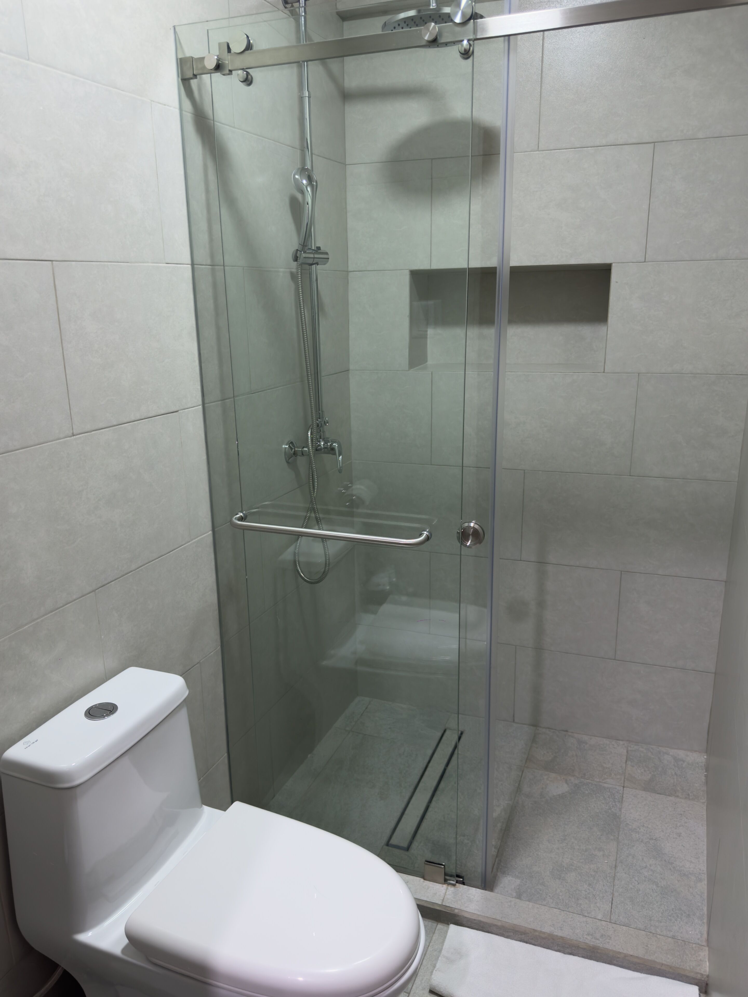 Une cabine de douche fermée par des parois en verre, équipée d’un pommeau de douche à main et d’un robinet à main.