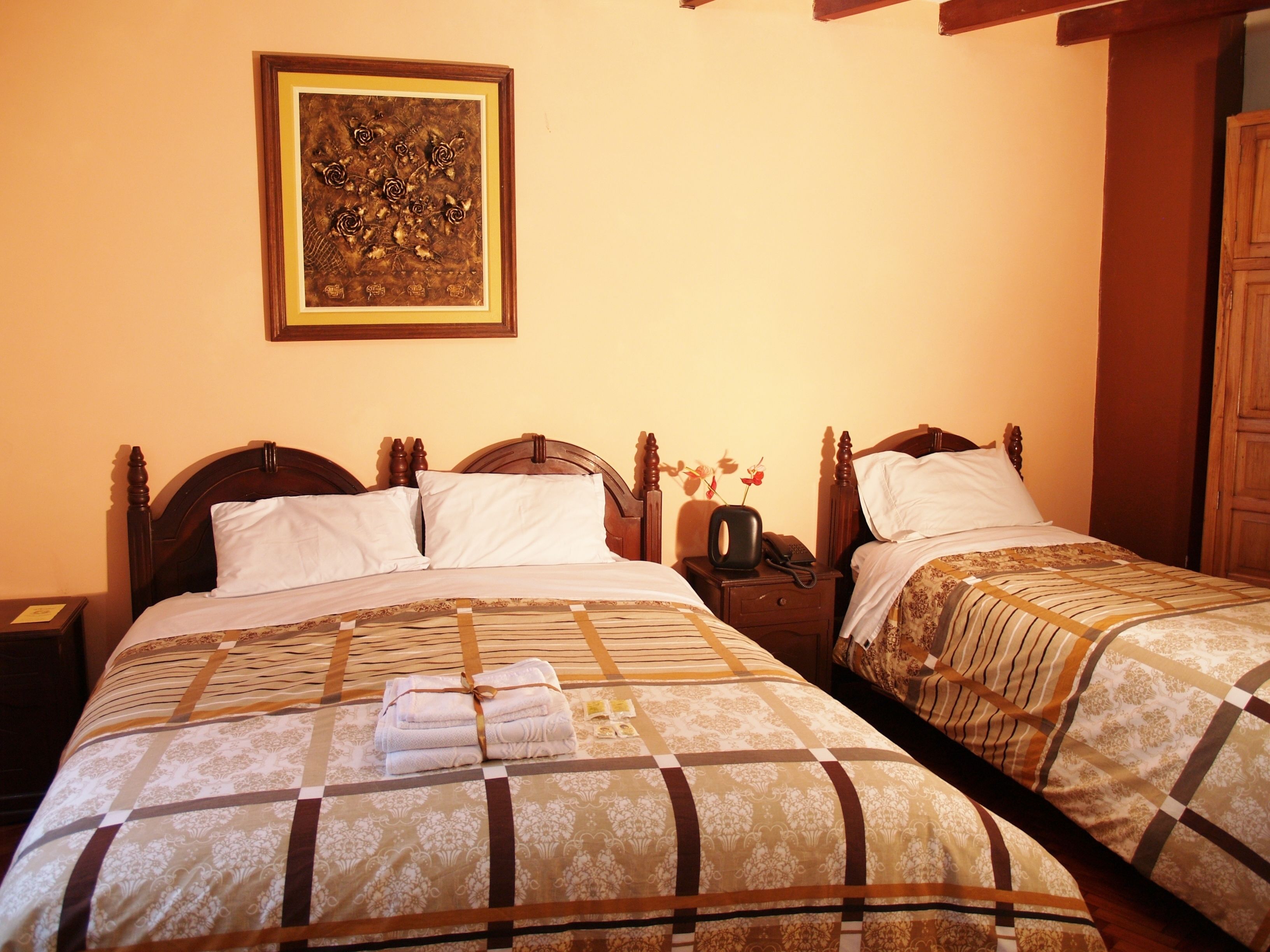 A hotel room with two wooden beds, a nightstand with a telephone, and a framed artwork on the wall.