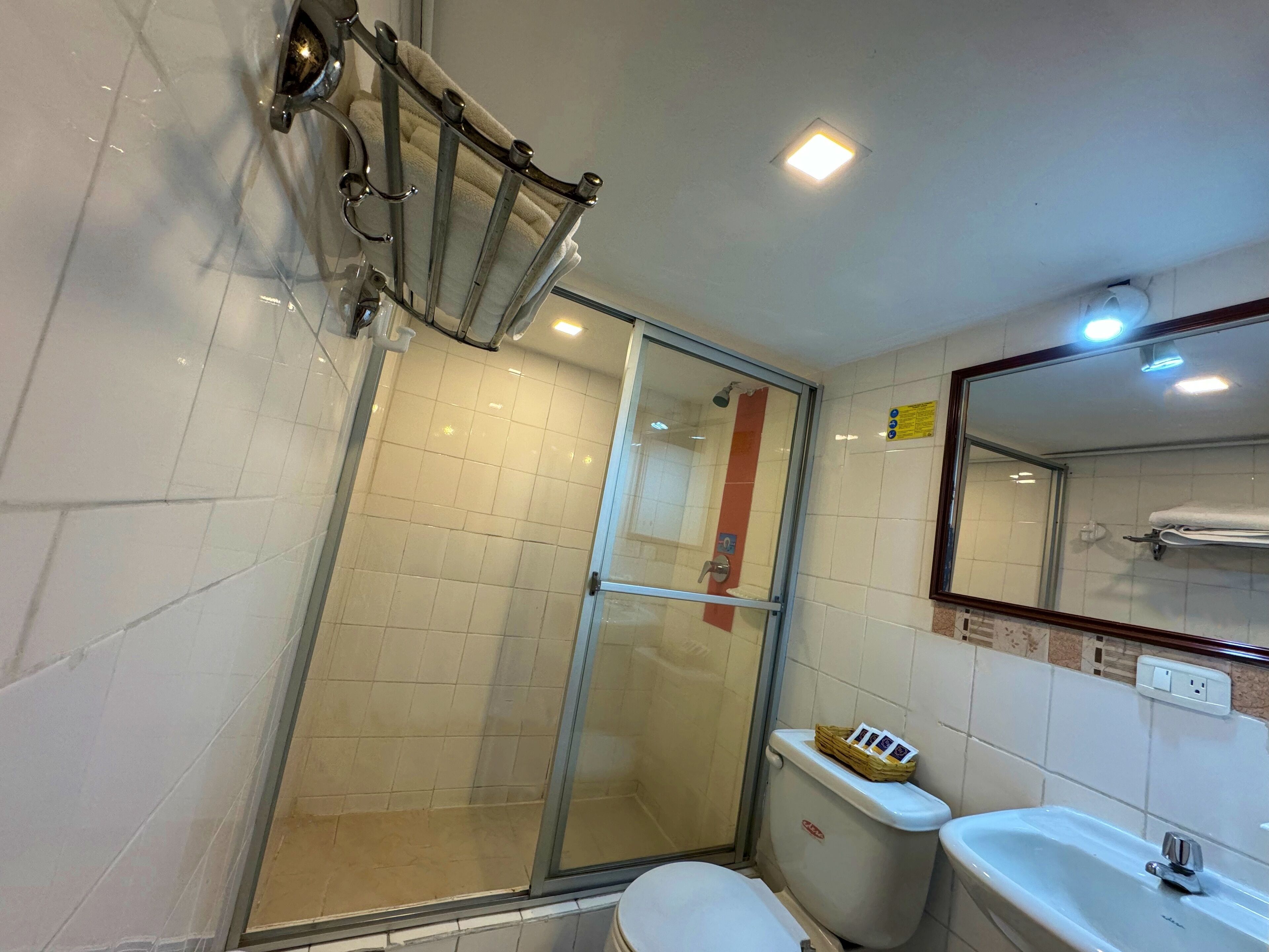 A bathroom with a glass shower enclosure, a toilet with a basket of toiletries, and a sink with a mirror above it.