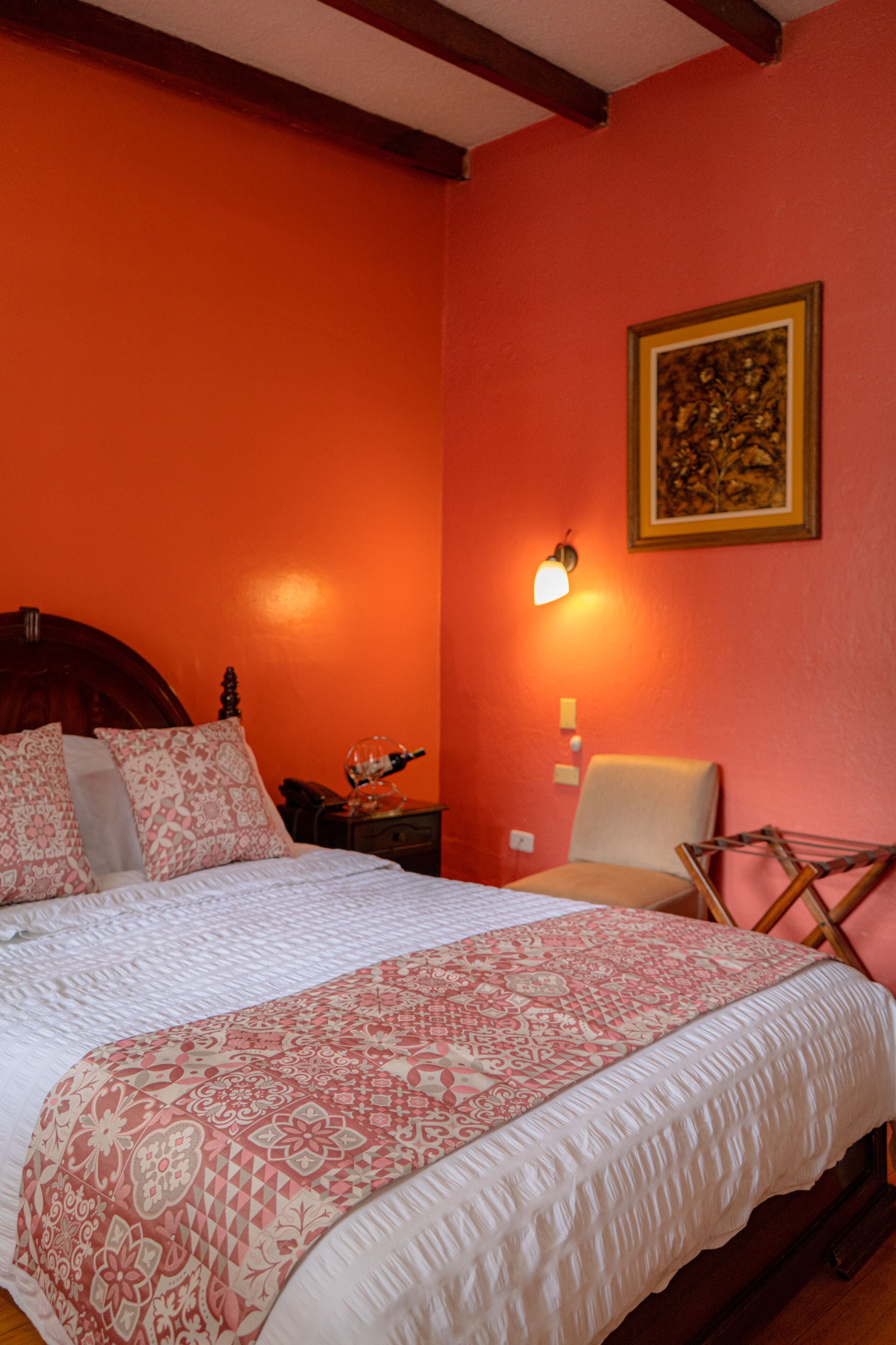 Un dormitorio con una cama, una silla, una mesita de noche y una lámpara de pared.