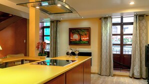 A modern kitchen with a central island, a dining area with a bench, and a large window with curtains. - Rincón Familiar Hotel Boutique (Quito)