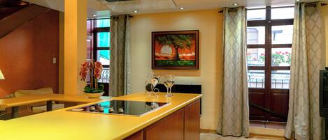 Una cocina moderna con una isla central, un comedor con banco y un amplio ventanal con cortinas.