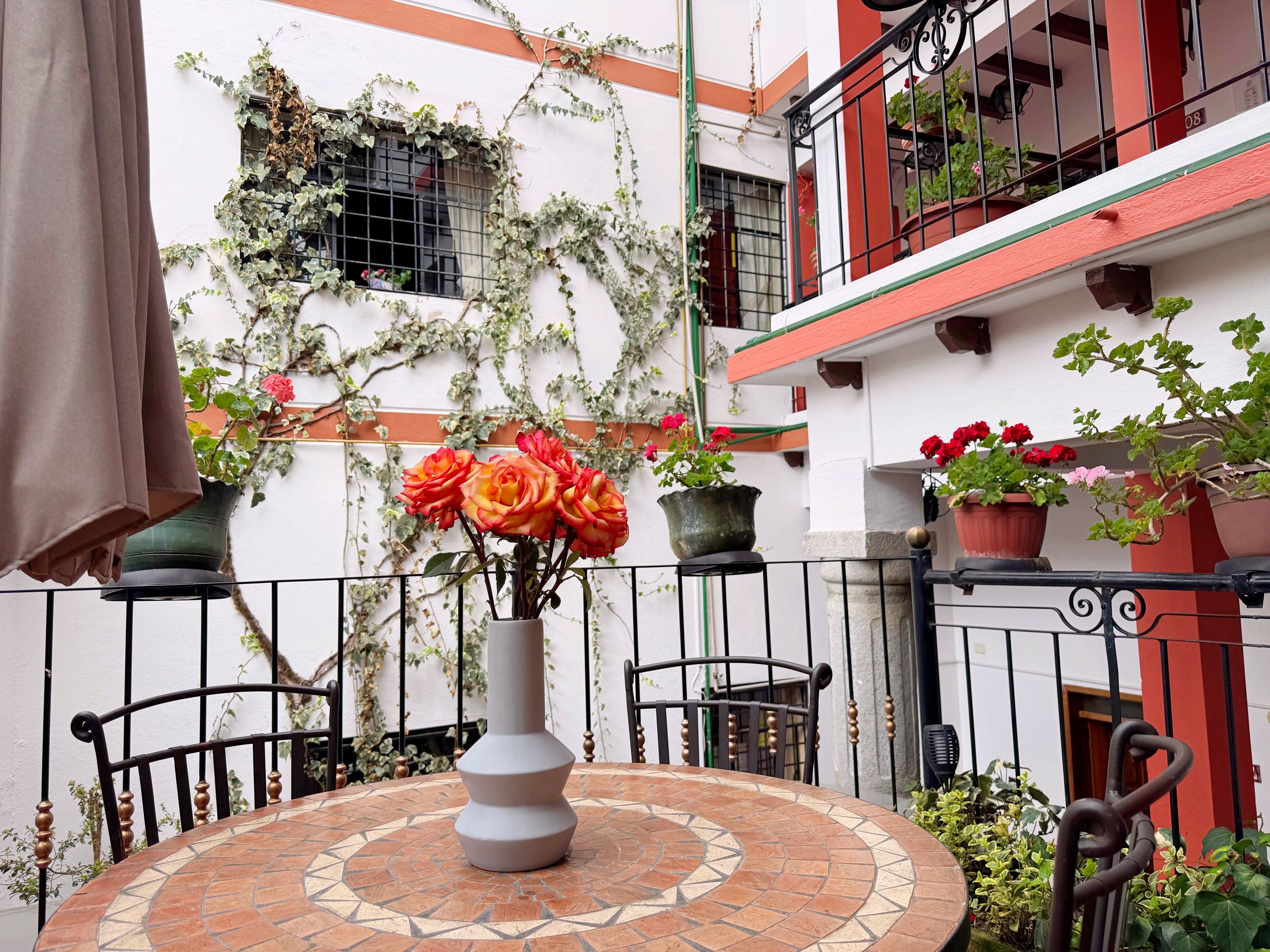 A patio with a tiled table, a vase with flowers, and potted plants.