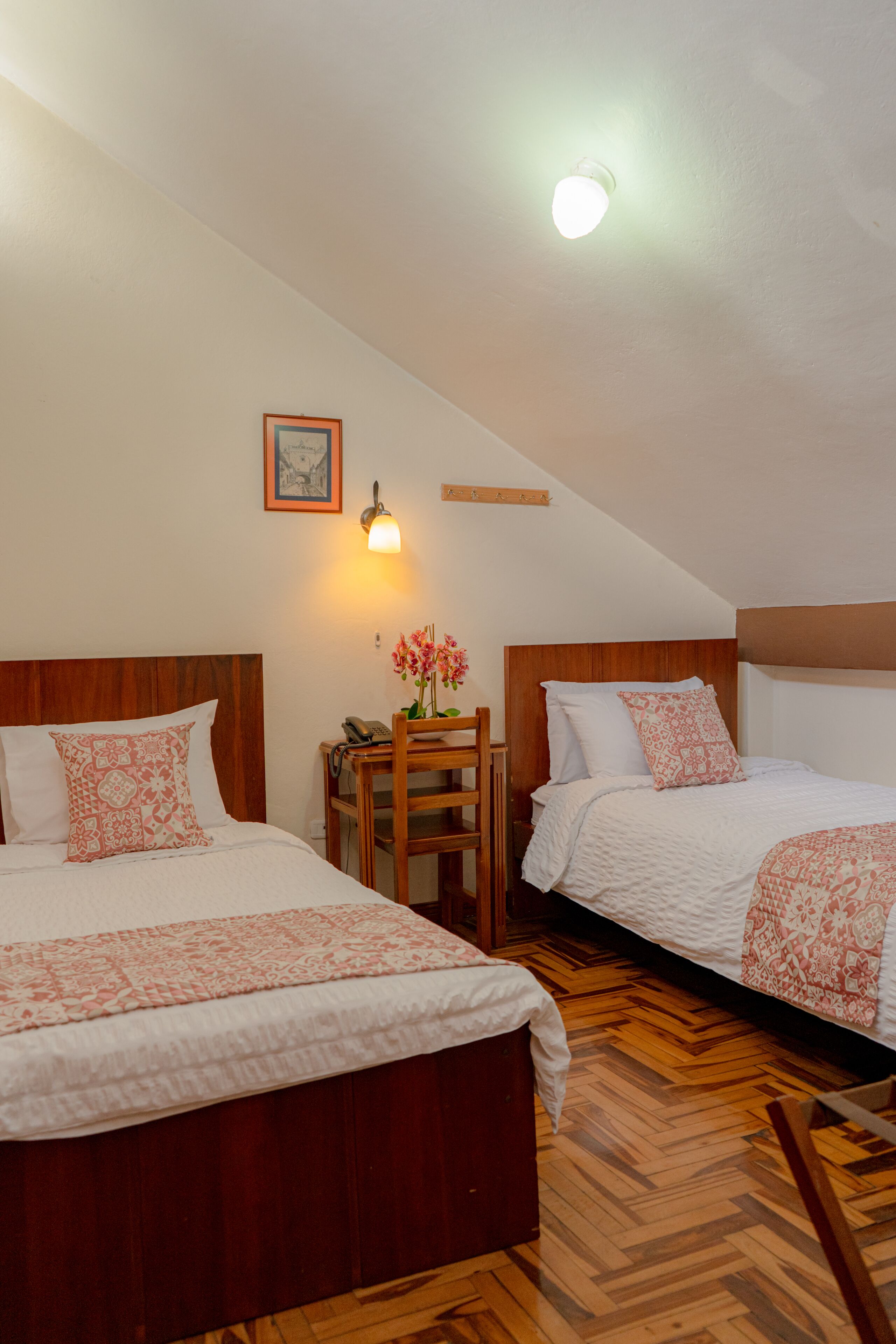 Una camera d'albergo con due letti, testiere in legno, un tavolino con una lampada e un quadro appeso al muro.