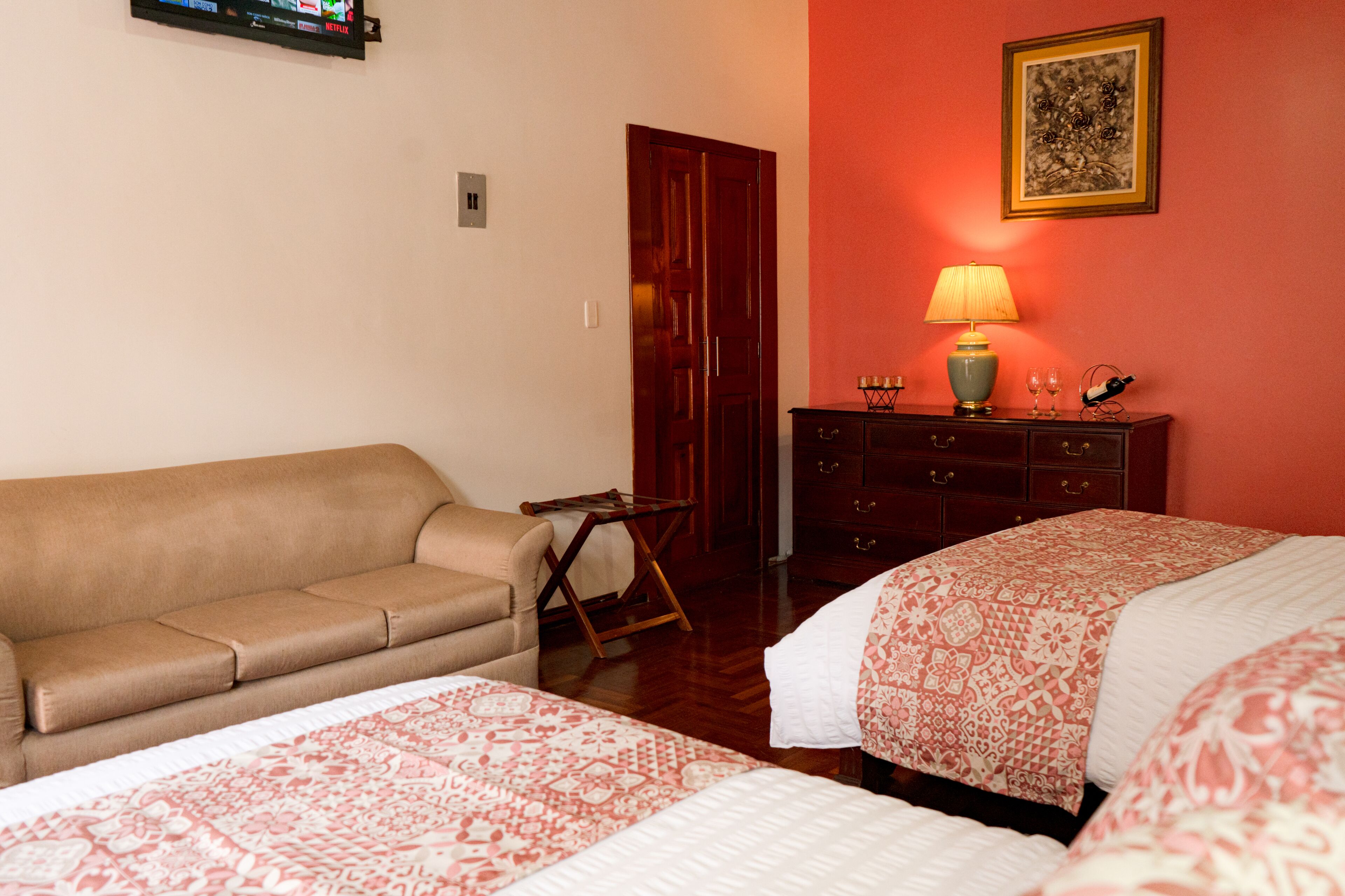 Une chambre d’hôtel avec un canapé, deux lits avec une literie à motifs, une commode en bois, une lampe et un tableau encadré au mur.