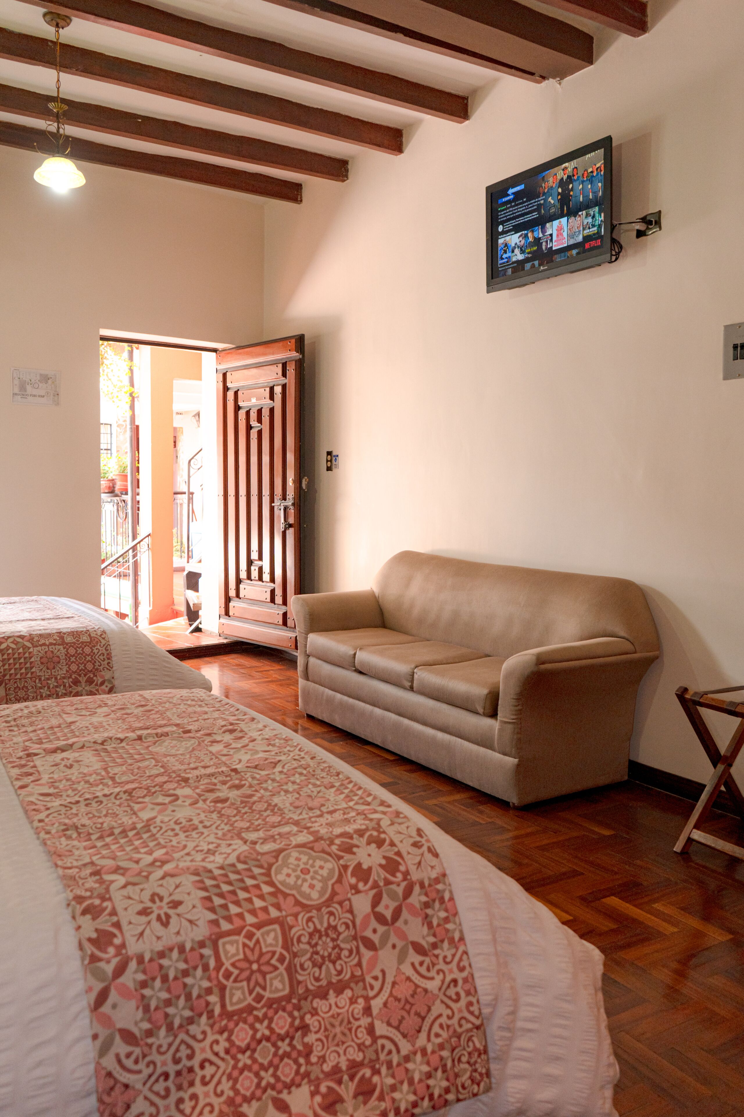 A room with a sofa, a bed with patterned bedding, a television mounted on the wall, and a wooden ceiling.
