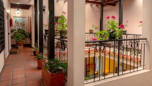 A corridor with potted plants, a tiled floor, and a balcony with a railing. - Rincón Familiar Hotel Boutique (Quito)