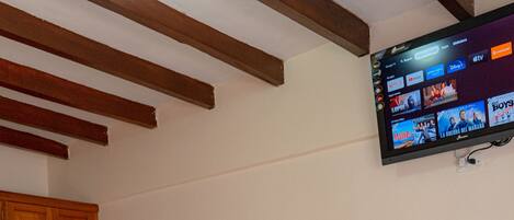 A bedroom with two beds, wooden wardrobe, and a mounted TV displaying various channels.
