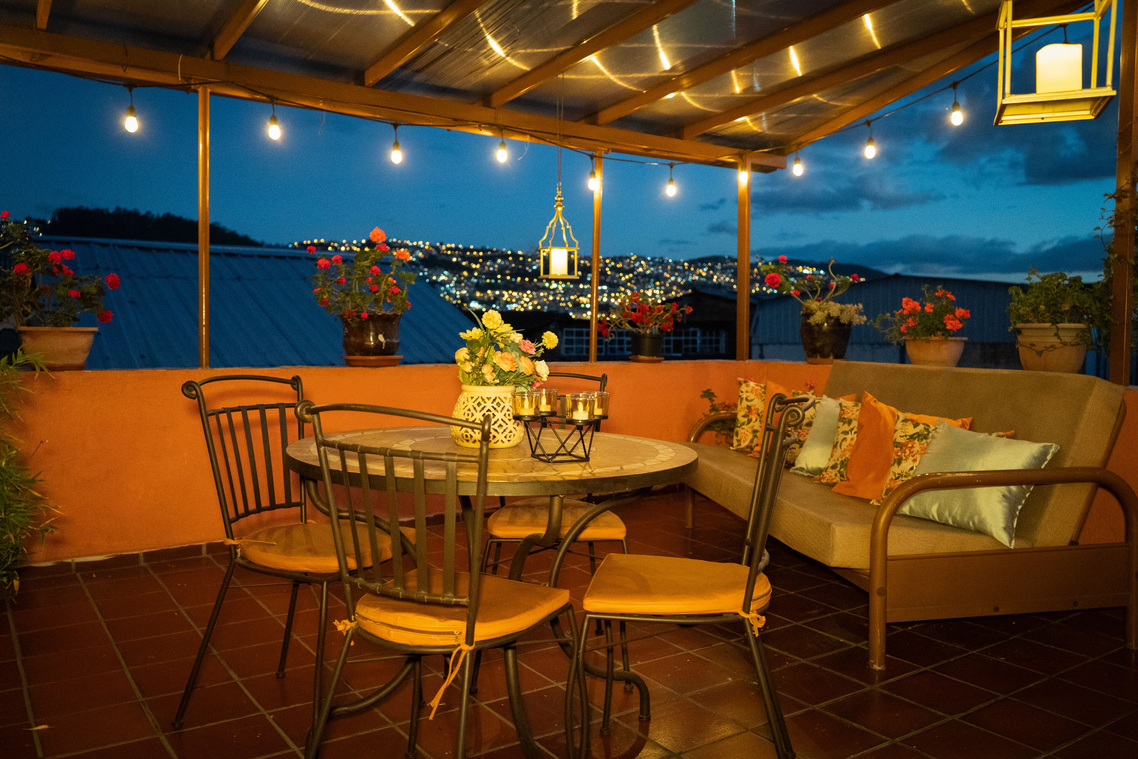 A covered patio with a round table and chairs, a sofa, and potted plants.
