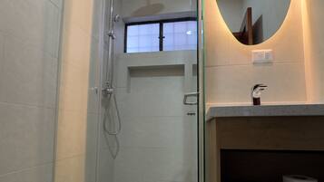 Un baño moderno con ducha de vidrio, inodoro, lavamanos con espejo y repisa con toallas.