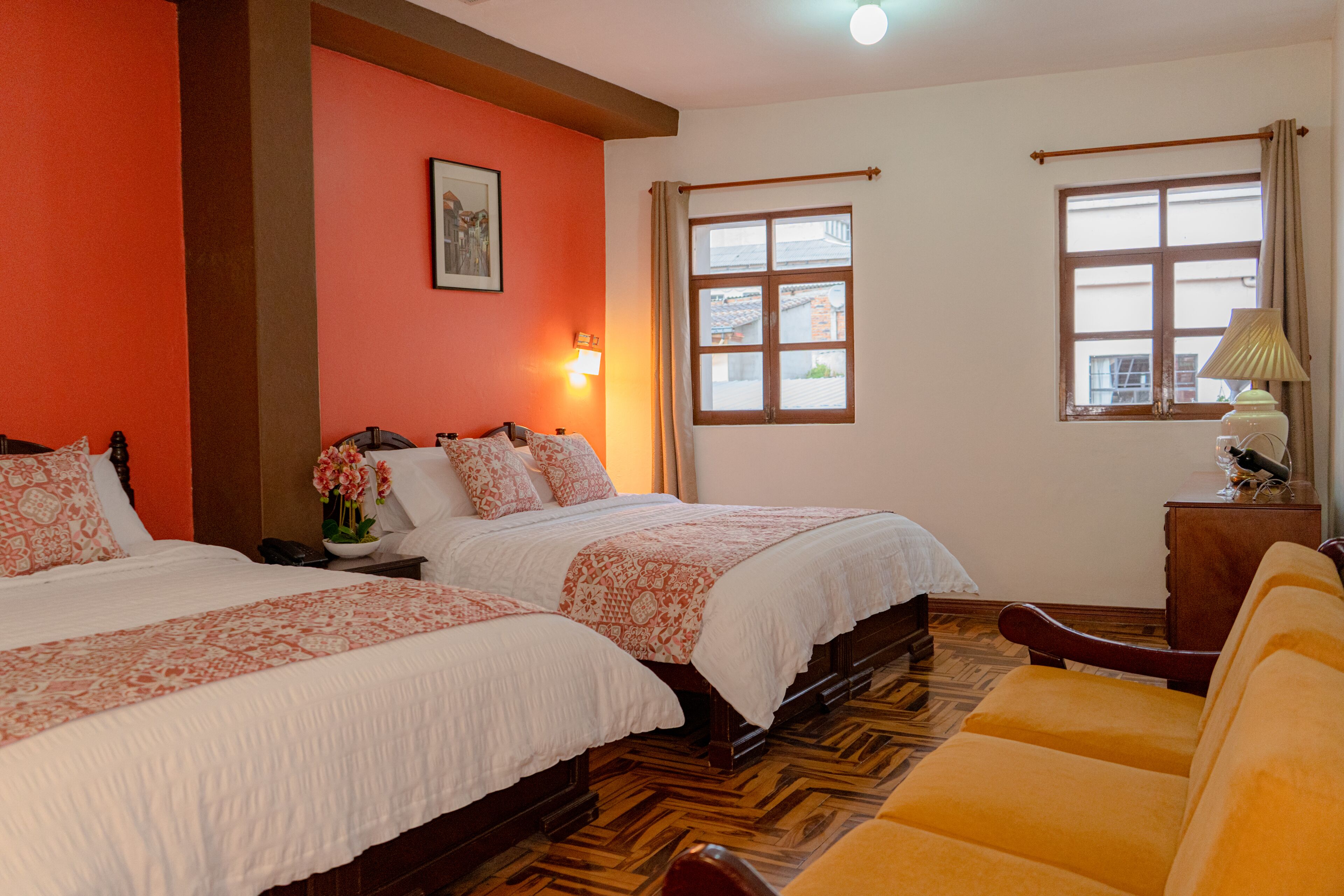 A hotel room with two beds, a wooden floor, a sofa, and a window with curtains.