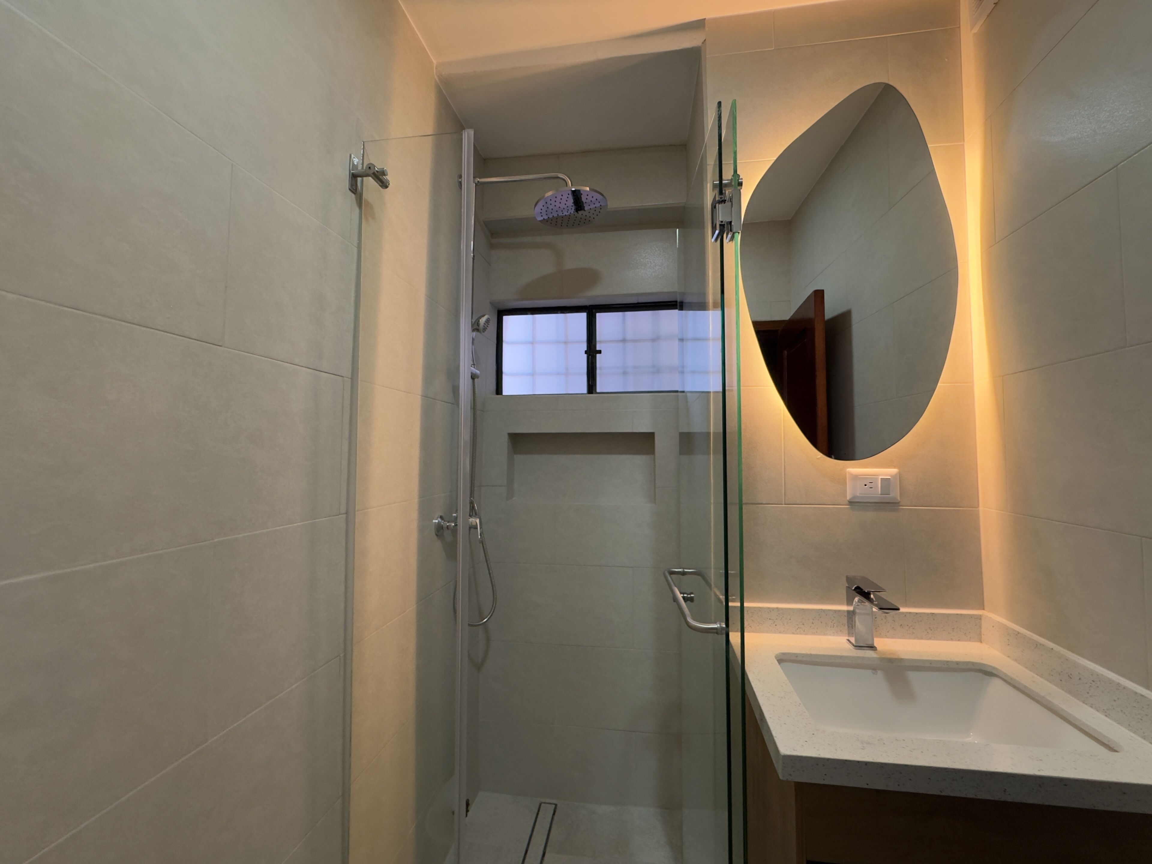 A modern bathroom with a glass shower enclosure, a sink, and a mirror.