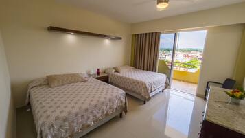 Habitación de hotel con dos camas, ventilador de techo, mesita de noche, escritorio y vista a la ciudad.