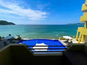 Piscina con vista al mar, sillas de descanso y un edificio amarillo.