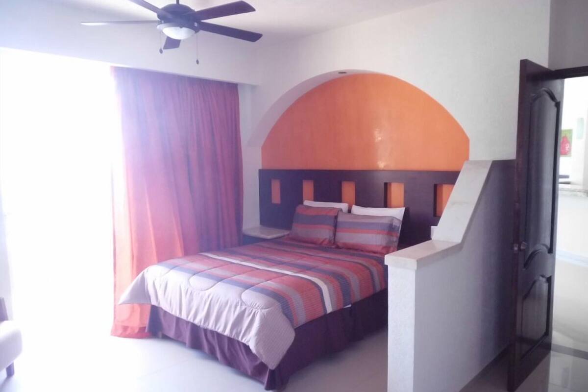 A bedroom with a bed, a ceiling fan, a window with curtains, and a door.