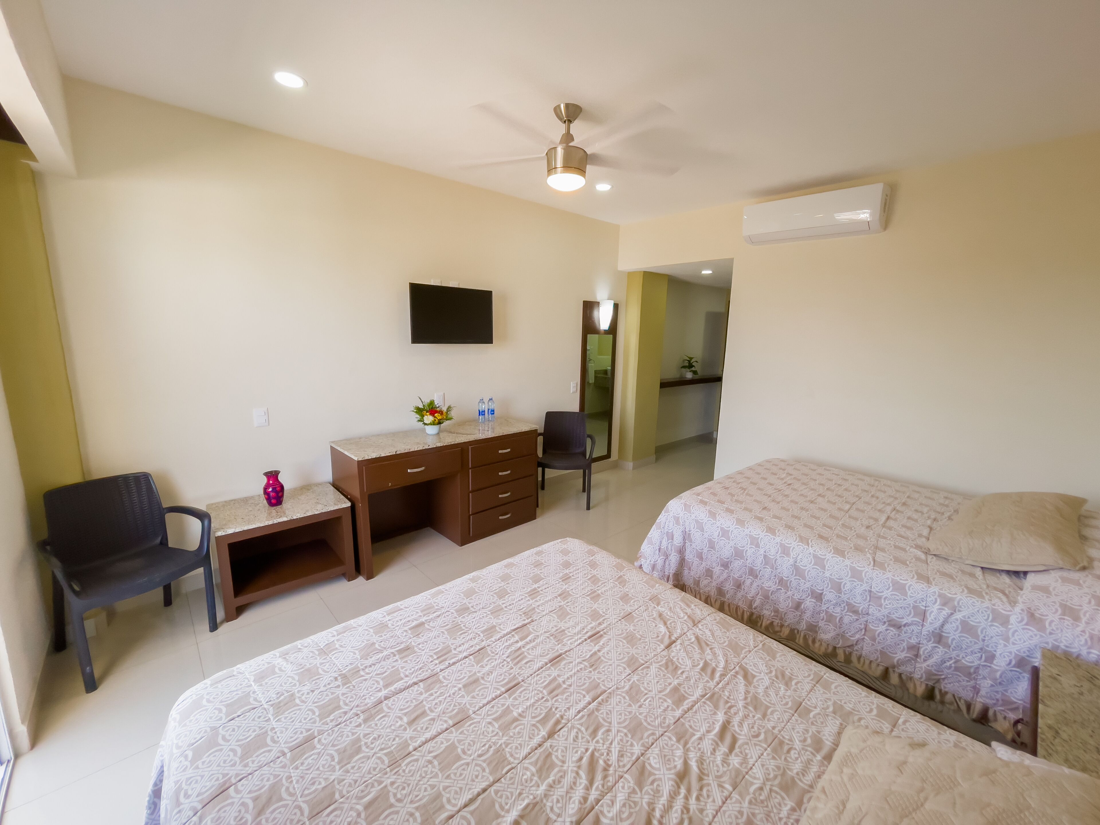 A hotel room with two beds, a desk with a chair, a TV, and an air conditioning unit.