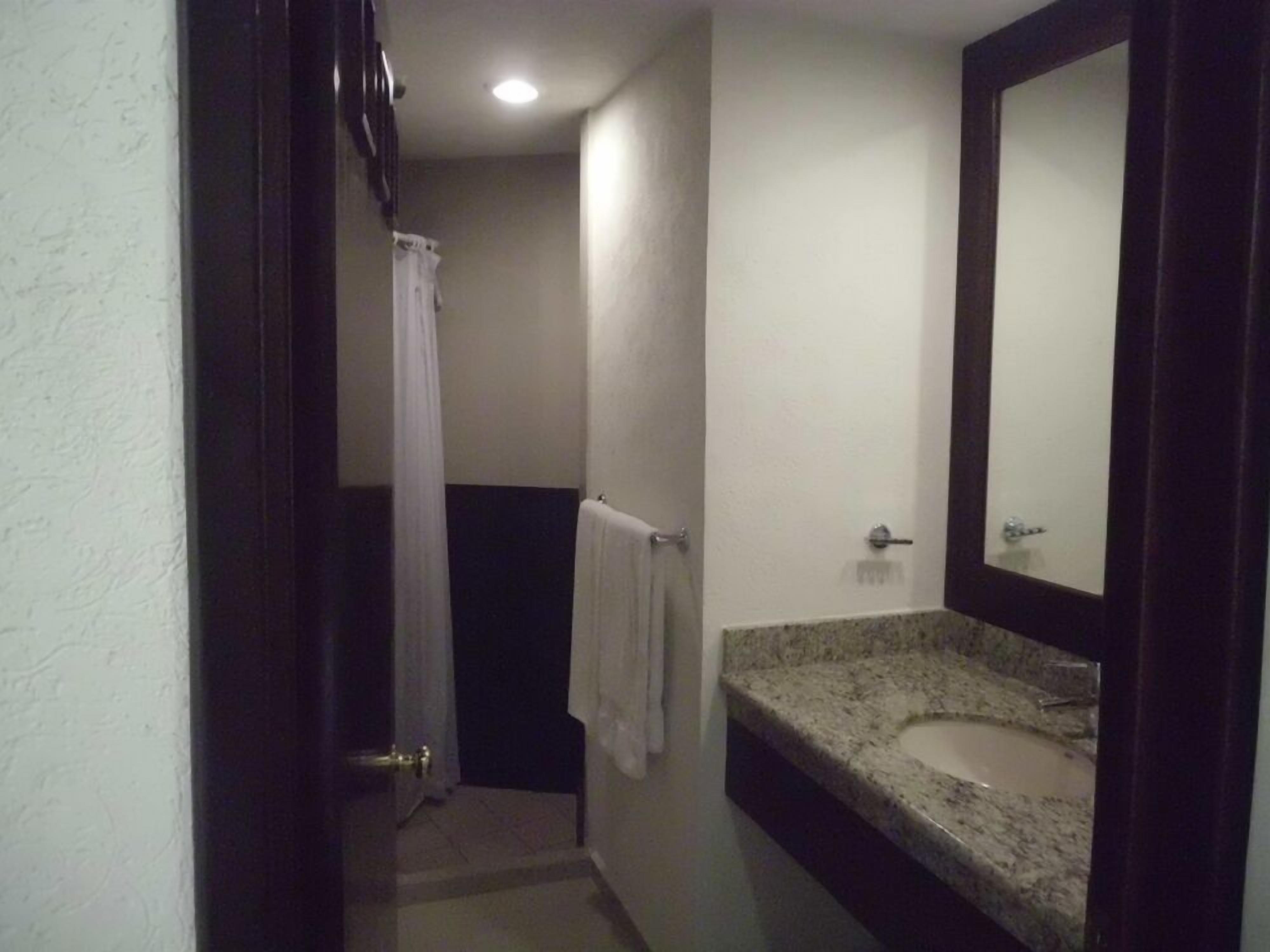 Un baño pequeño con lavamanos de granito, un espejo y una cortina de ducha.
