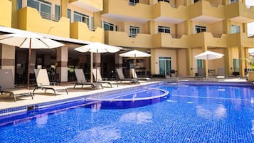 Zona de piscina de hotel con varios niveles, sillas de descanso y sombrillas.