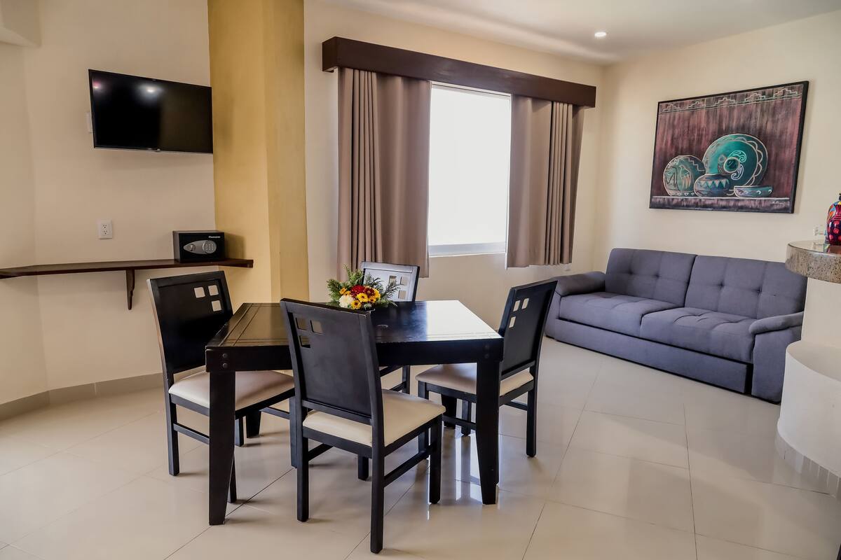 A modern living room with a dining table, chairs, a sofa, a TV, and a painting on the wall.