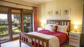 Un dormitorio con una cama de madera, dos mesitas de noche con lámparas, un ventanal corredero a un balcón y tres cuadros enmarcados en la pared.