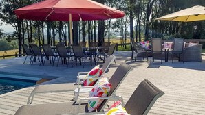 Zona junto a la piscina con sillones de descanso y sombrillas, una piscina y vistas a árboles y colinas.